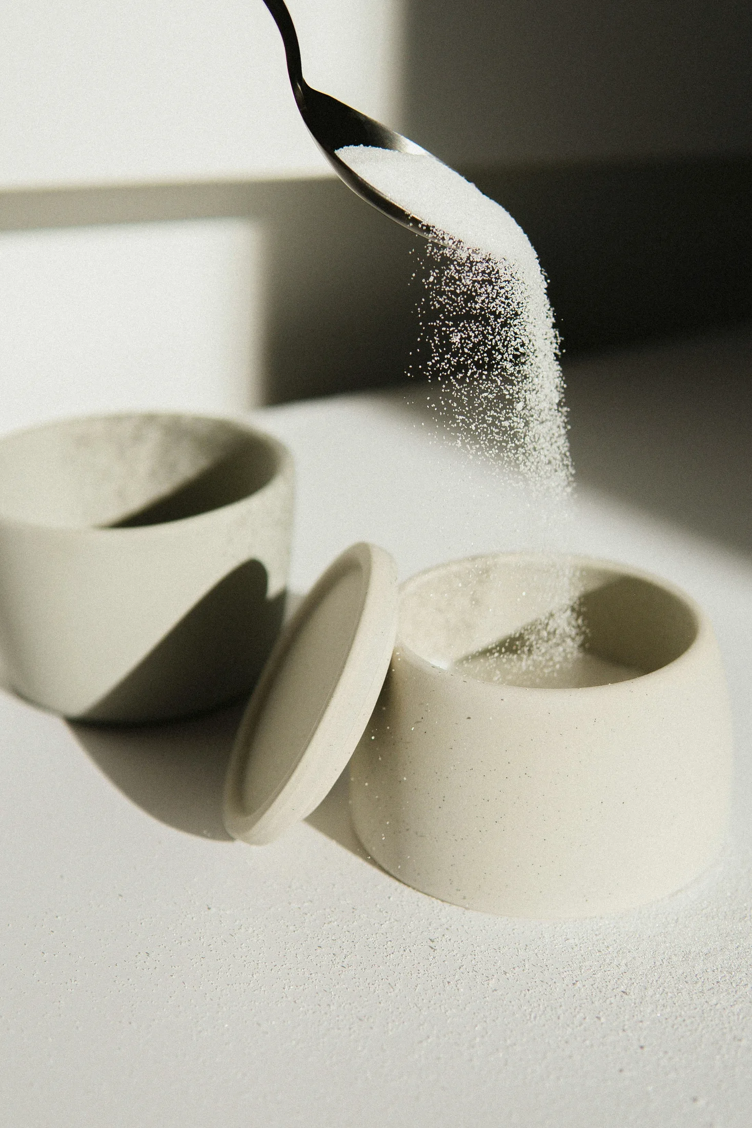A spoon pouring sugar in to a sugar bowl 