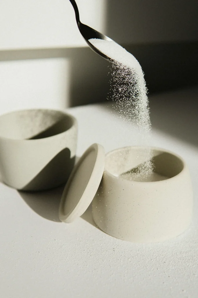 A spoon pouring sugar in to a sugar bowl